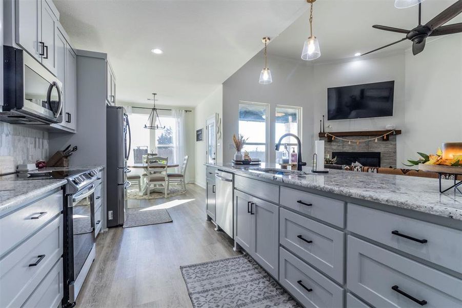 Kitchen with stainless steel appliances, light stone counters, sink, and decorative light fixtures