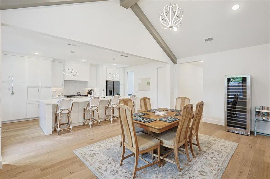 Dining space with light hardwood / wood-style floors, beam ceiling, a notable chandelier, beverage cooler, and high vaulted ceiling