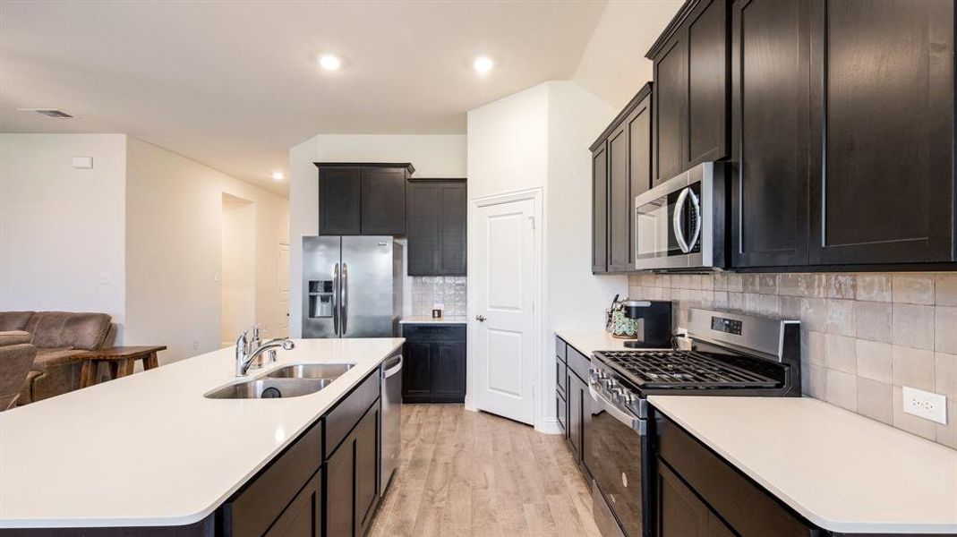 Kitchen featuring appliances with stainless steel finishes, light hardwood / wood-style flooring, tasteful backsplash, sink, and an island with sink
