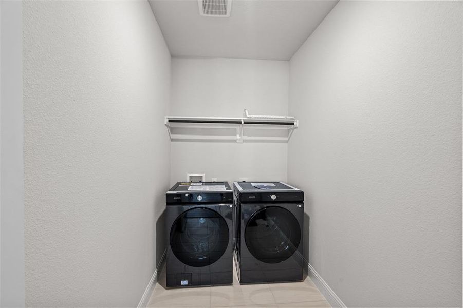 Clothes washing area with light tile patterned flooring and independent washer and dryer