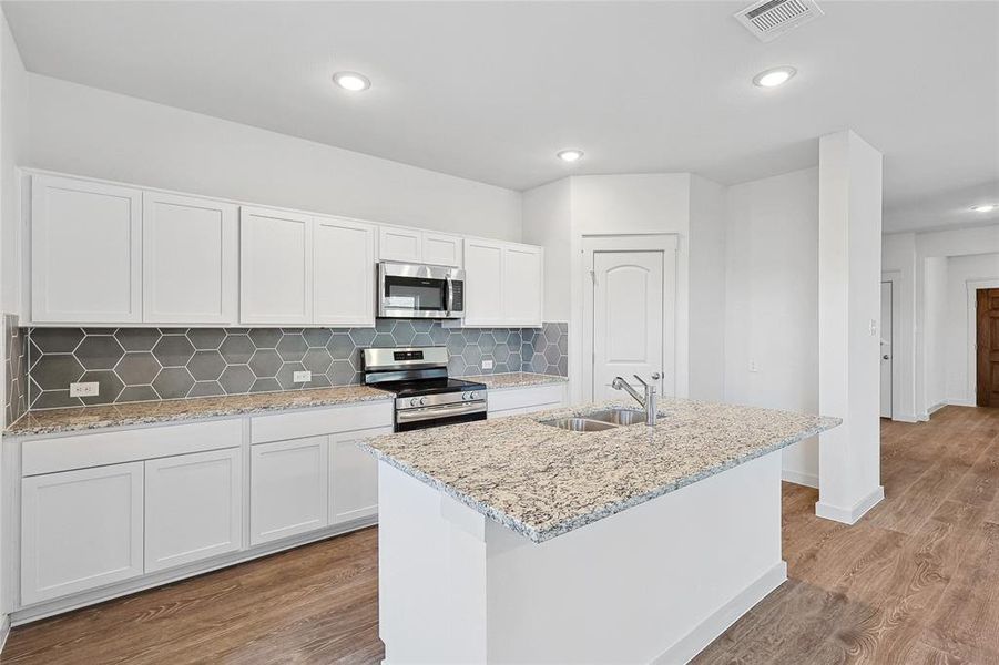 Kitchen featuring light wood-type flooring, sink, white cabinetry, a center island with sink, and appliances with stainless steel finishes