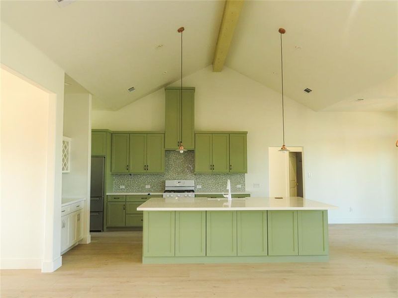 Kitchen with high vaulted ceiling, beam ceiling, light hardwood / wood-style floors, and a kitchen island with sink