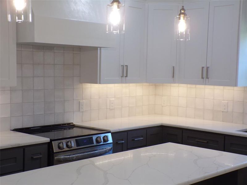 Kitchen with electric stove, light stone counters, and white cabinetry