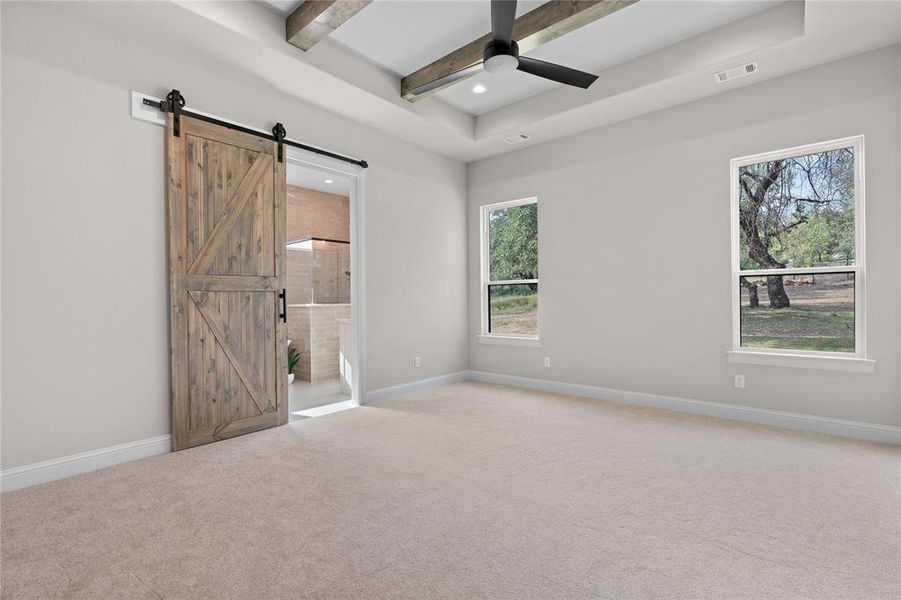 Carpeted spare room with a barn door, beamed ceiling, plenty of natural light, and ceiling fan