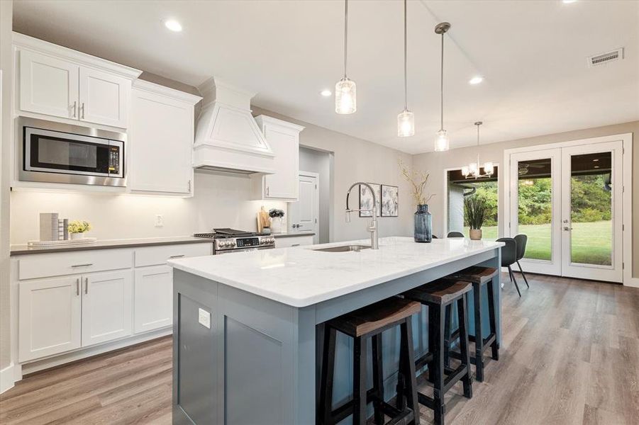 Kitchen featuring premium range hood, appliances with stainless steel finishes, light hardwood / wood-style floors, sink, and a center island with sink