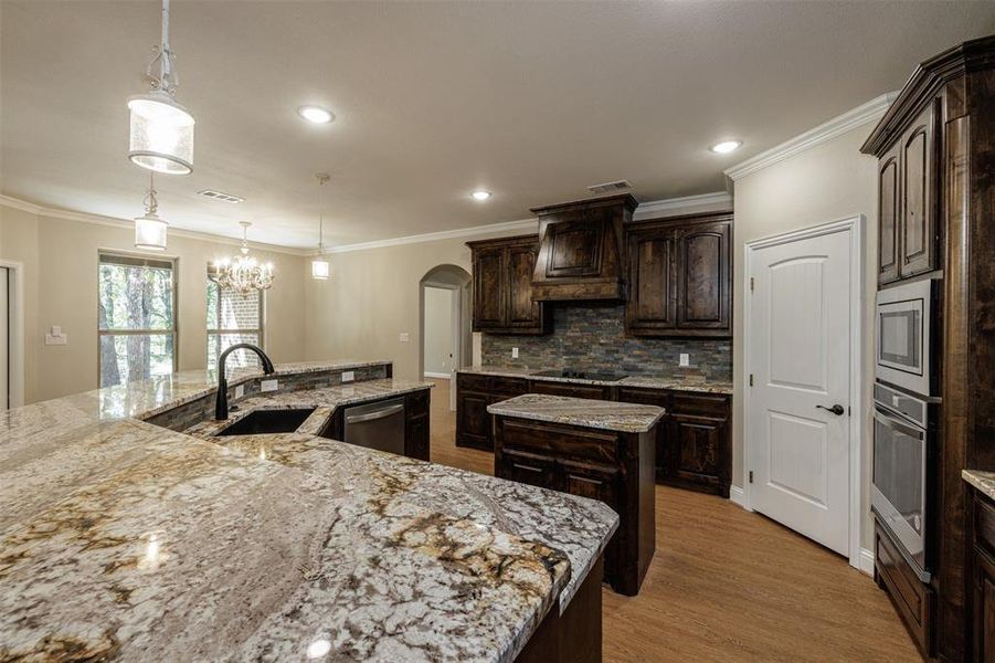 Kitchen featuring pendant lighting, stainless steel appliances, crown molding, dark brown cabinets, and a center island