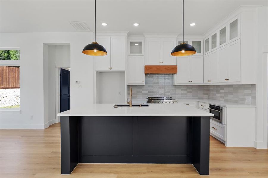 Kitchen featuring a kitchen island with sink, sink, pendant lighting, and white cabinetry