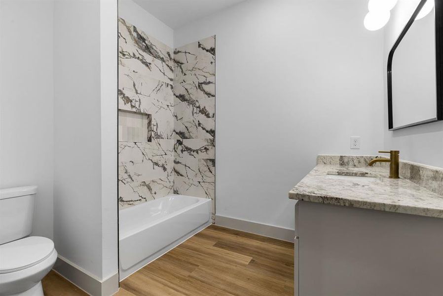 Full bathroom with toilet, vanity, tiled shower / bath combo, and hardwood / wood-style flooring