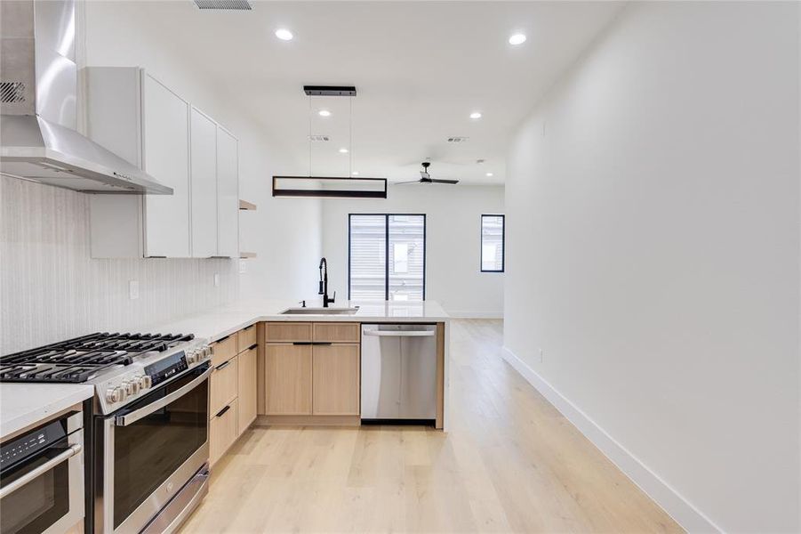 Kitchen with light brown cabinets, sink, kitchen peninsula, wall chimney exhaust hood, and appliances with stainless steel finishes