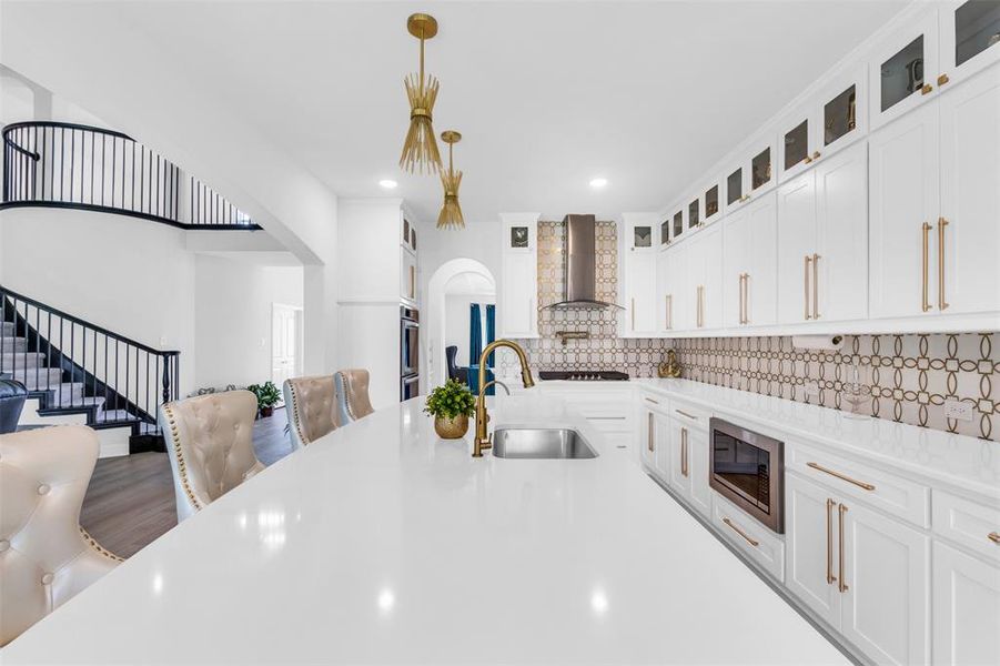 Kitchen featuring stainless steel appliances, hanging light fixtures, backsplash, white cabinetry, and wall chimney exhaust hood