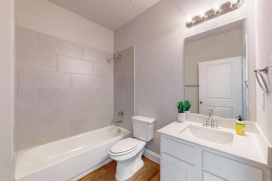 Full bathroom featuring vanity, tiled shower / bath combo, hardwood / wood-style flooring, and toilet