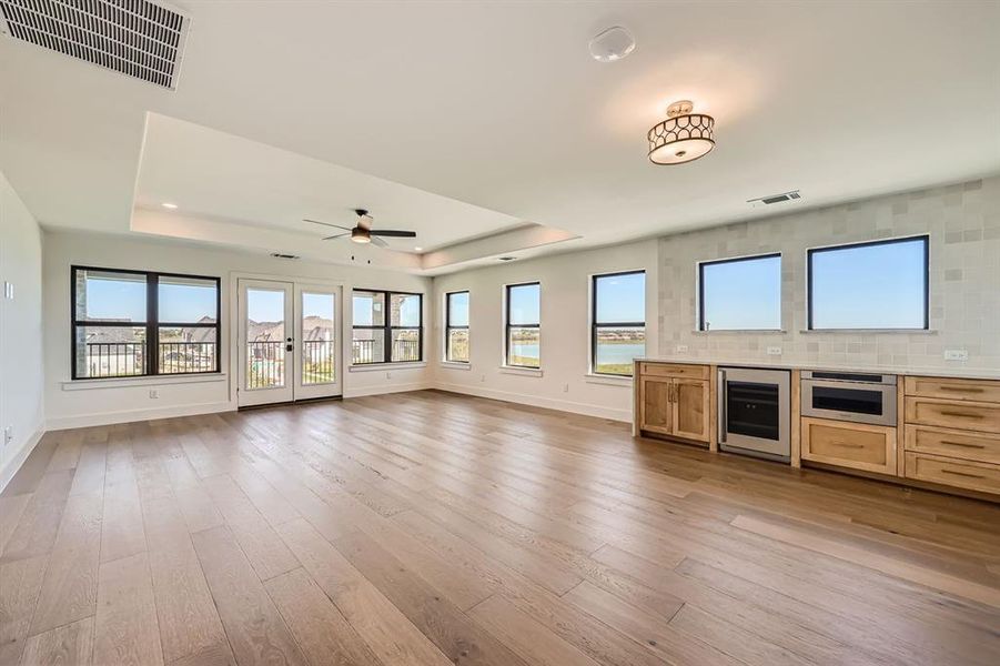 Unfurnished living room featuring a tray ceiling, beverage cooler, ceiling fan, and light hardwood / wood-style floors