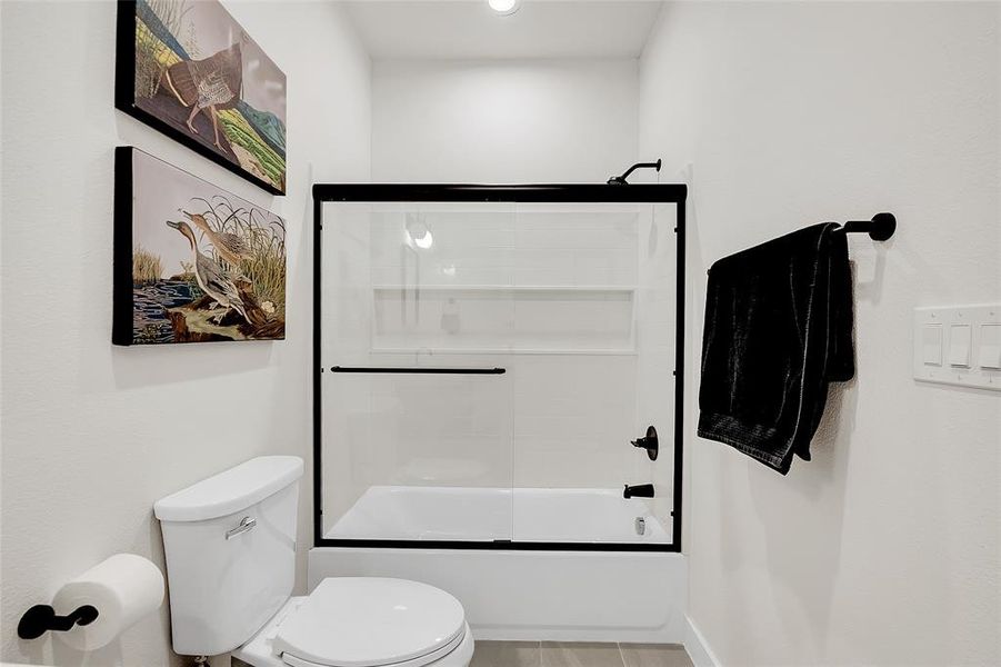 Shared Bathroom featuring tile patterned floors, bath / shower combo with glass door, and toilet