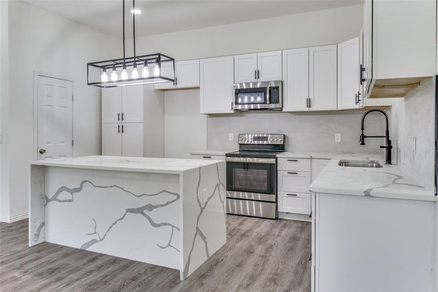 Kitchen featuring light hardwood / wood-style flooring, stainless steel appliances, white cabinets, decorative light fixtures, and backsplash