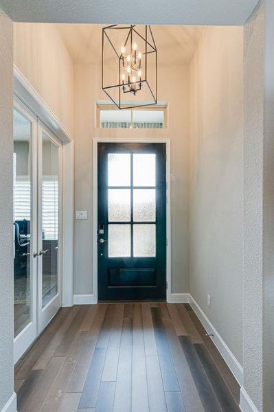 Entryway with a notable chandelier, french doors to office, and hardwood flooring.
