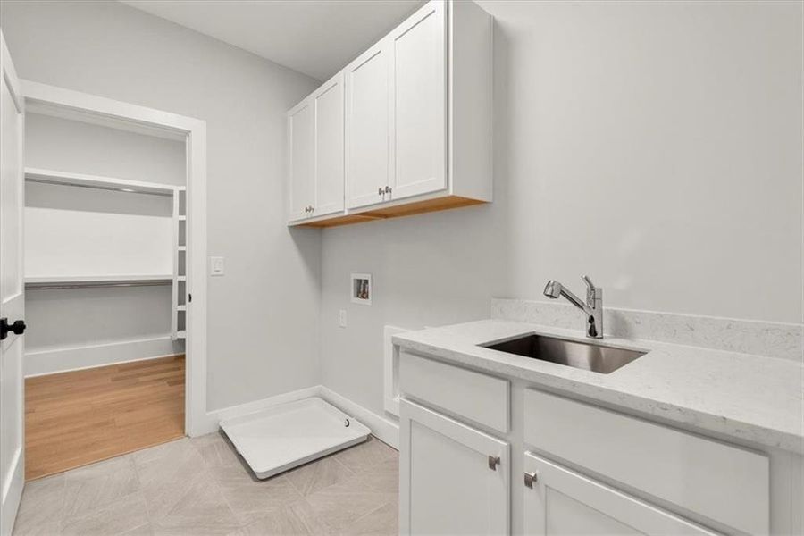 Washroom featuring light tile flooring, sink, cabinets, and washer hookup