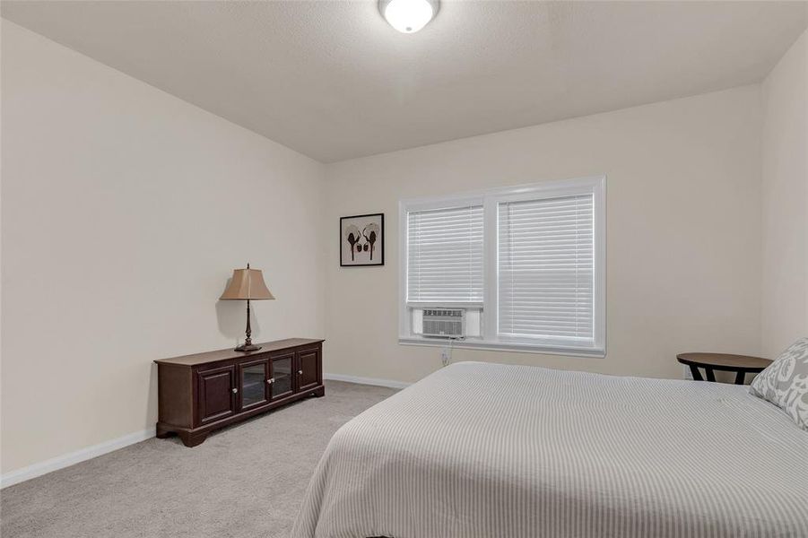 This is a well-lit, neutral-toned bedroom. The room has carpet flooring and a simple, clean design.