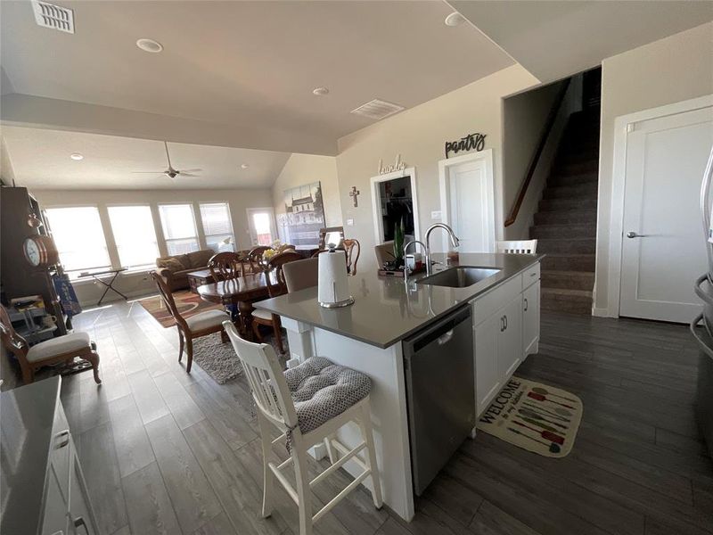 Kitchen with an island with sink, stainless steel dishwasher, white cabinetry, a kitchen breakfast bar, and vaulted ceiling