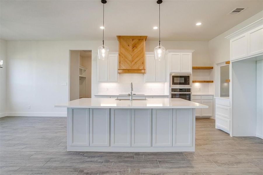 Kitchen with a center island with sink, appliances with stainless steel finishes, decorative light fixtures, and white cabinets