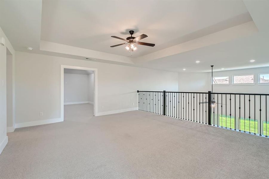 Spare room with ceiling fan, a raised ceiling, and light colored carpet