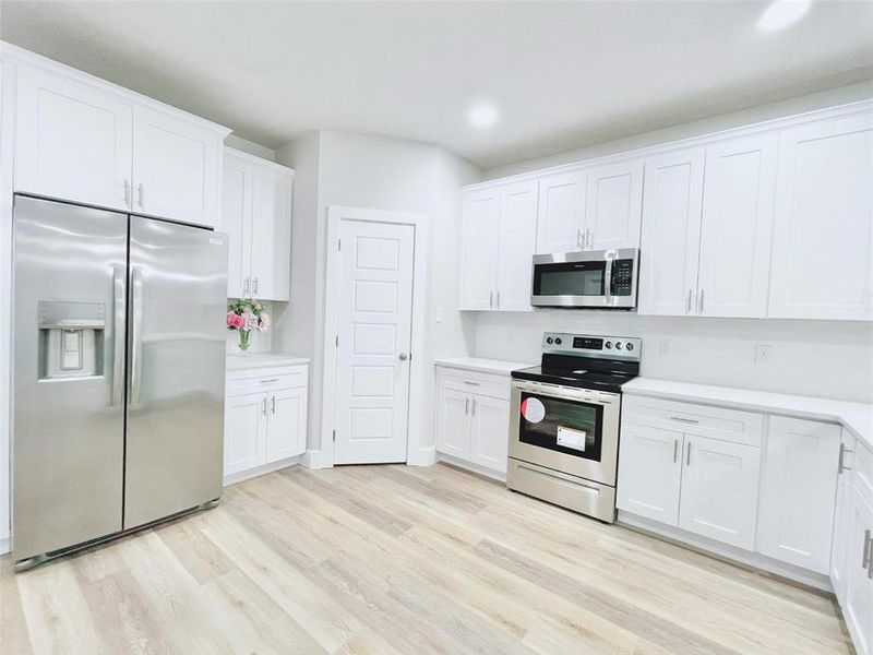 Kitchen featuring light wood-type flooring, white cabinetry, and appliances with stainless steel finishes