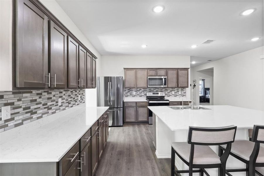 Kitchen with tasteful backsplash, stainless steel appliances, a kitchen island with sink, sink, and dark hardwood / wood-style floors