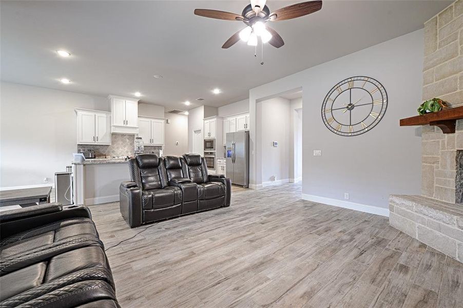 Living room with a fireplace, light wood-type flooring, and ceiling fan