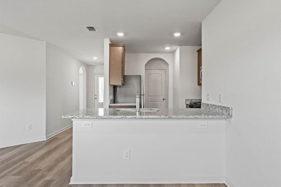 Kitchen featuring stainless steel fridge, light wood-type flooring, kitchen peninsula, light stone counters, and sink