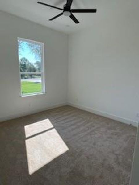 Empty room featuring dark colored carpet and ceiling fan