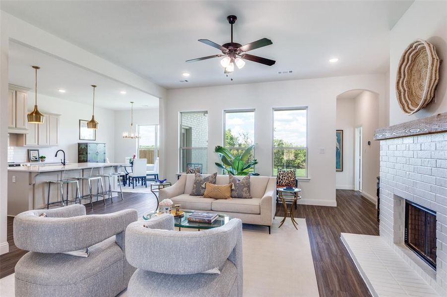 Living room with ceiling fan with notable chandelier, dark hardwood / wood-style flooring, a brick fireplace, and sink