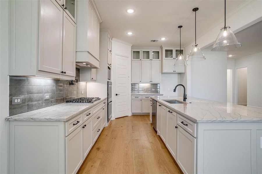 Kitchen with white cabinetry, backsplash, light hardwood / wood-style floors, light stone countertops, and sink