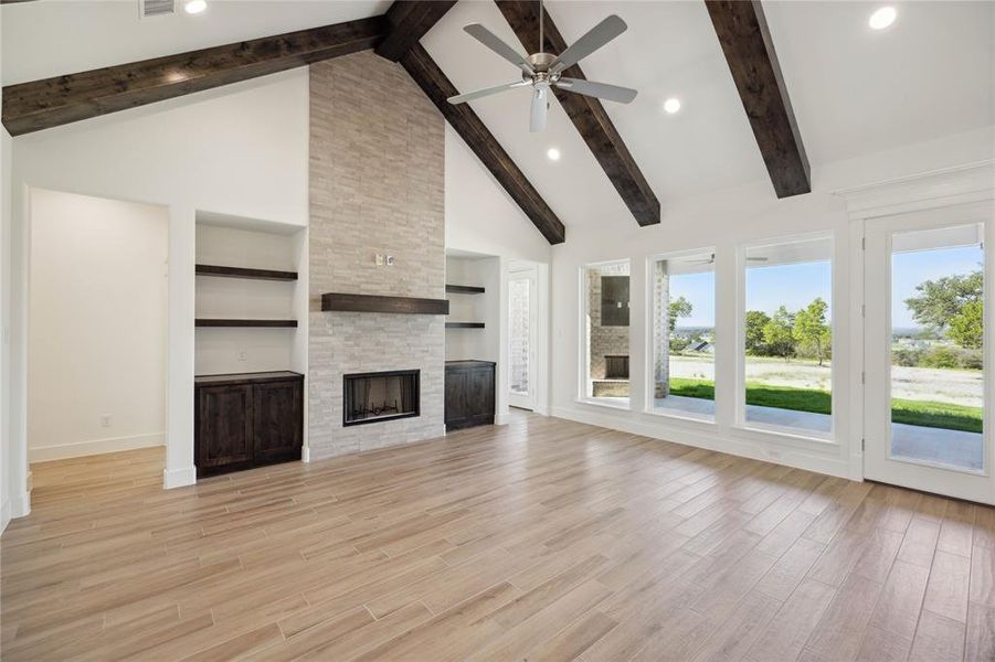 Unfurnished living room with a stone fireplace, high vaulted ceiling, light hardwood / wood-style floors, beamed ceiling, and ceiling fan