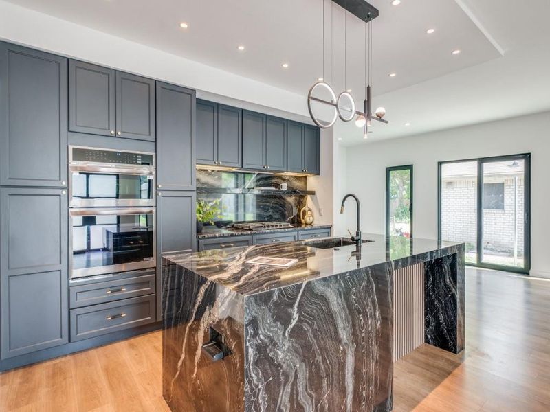 Kitchen with hanging light fixtures, a large island, stainless steel double oven, dark stone counters, and sink