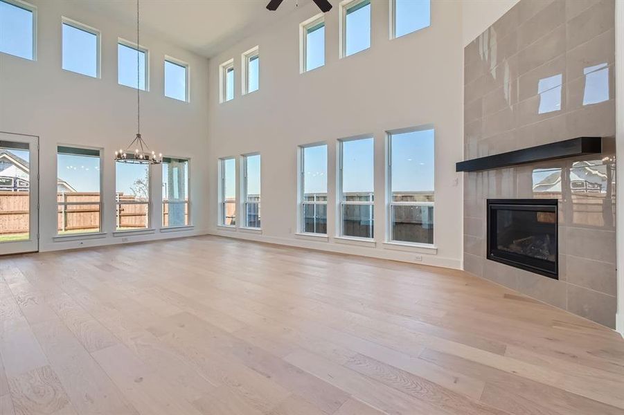 Unfurnished living room with a tiled fireplace, a towering ceiling, light hardwood / wood-style flooring, and ceiling fan with notable chandelier