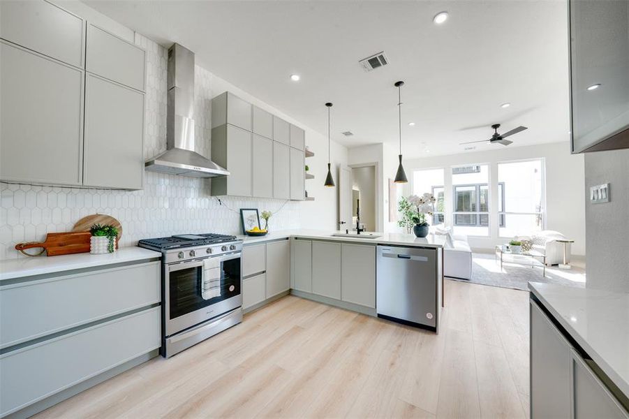 Kitchen featuring wall chimney range hood, stainless steel appliances, sink, decorative light fixtures, and light wood-type flooring