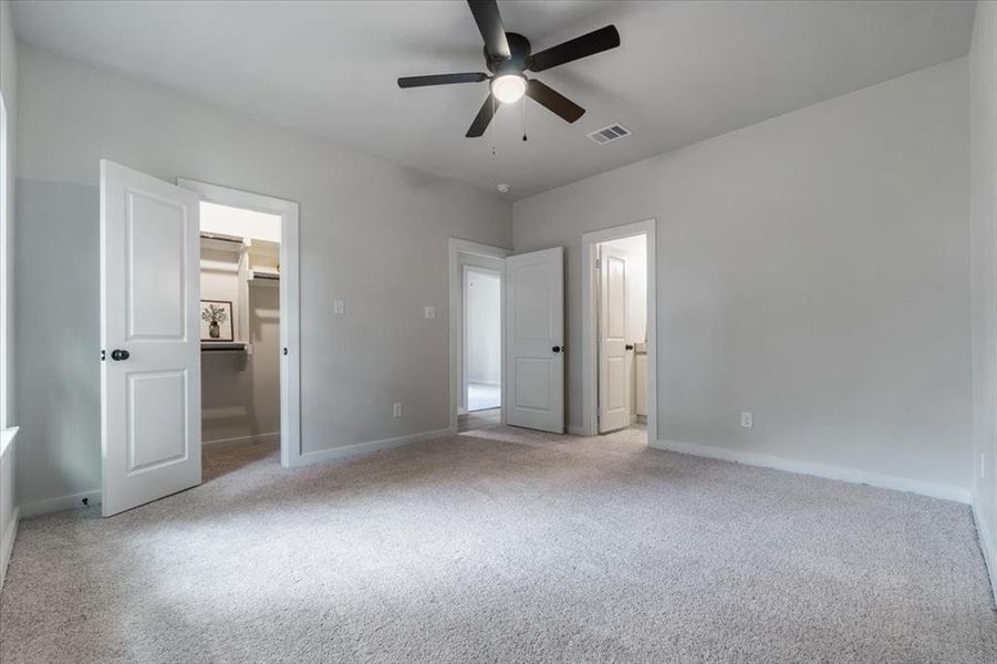 Unfurnished bedroom with a walk in closet, ceiling fan, and light colored carpet