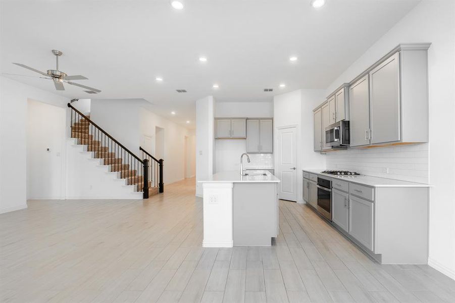 Kitchen featuring light hardwood / wood-style floors, a kitchen island with sink, stainless steel appliances, and gray cabinetry