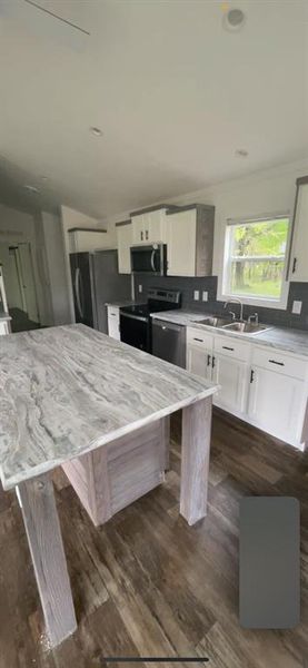 Kitchen featuring dark hardwood / wood-style flooring, appliances with stainless steel finishes, a center island, sink, and white cabinetry