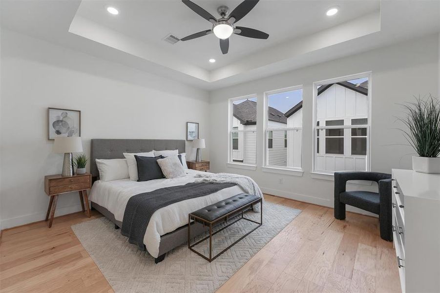 Step into your Owners Retreat, and well-lit -primary bedroom located on the 3rd floor features engineered hardwood floors, a high ceiling with a modern fan, large windows providing ample natural light, and a contemporary design aesthetic.