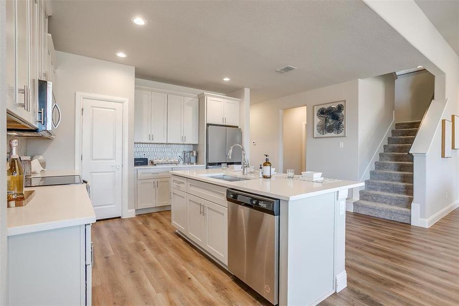 Kitchen with appliances with stainless steel finishes, white cabinetry, an island with sink, light hardwood / wood-style flooring, and sink