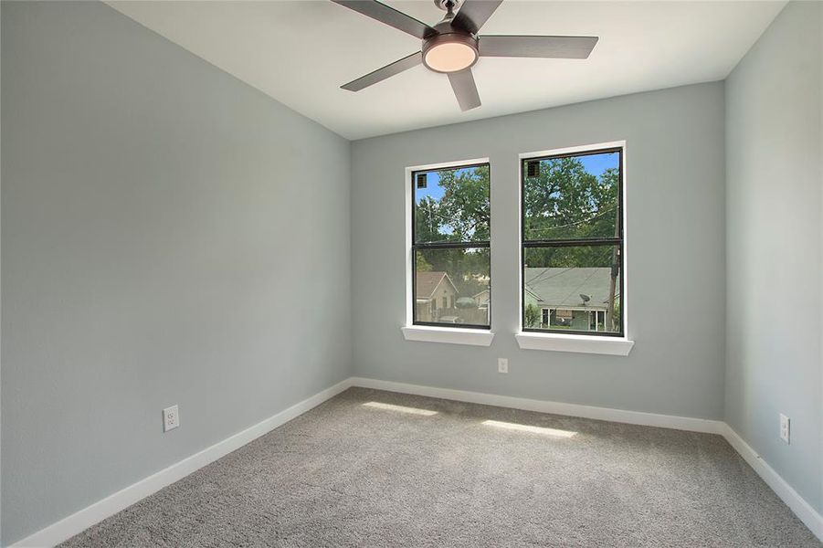 Carpeted empty room featuring ceiling fan and a wealth of natural light