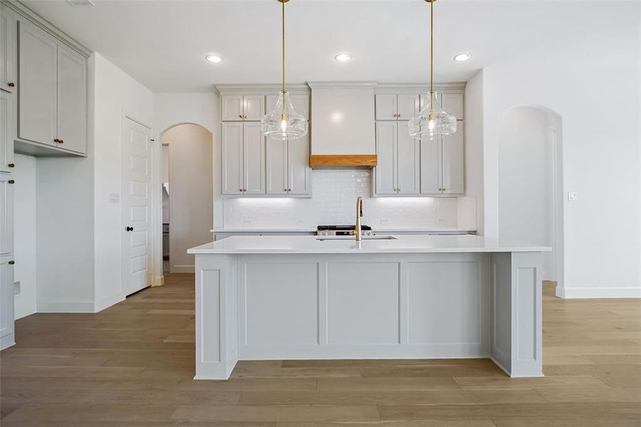 Kitchen featuring an island with sink, backsplash, sink, decorative light fixtures, and light hardwood / wood-style floors