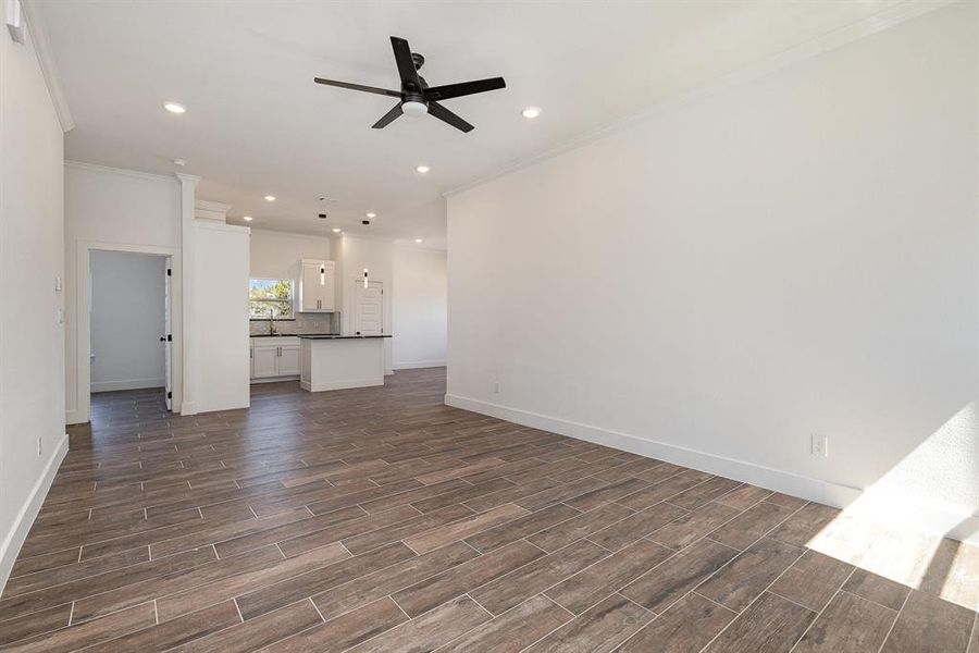 Unfurnished living room featuring ornamental molding, ceiling fan, and dark wood-type flooring