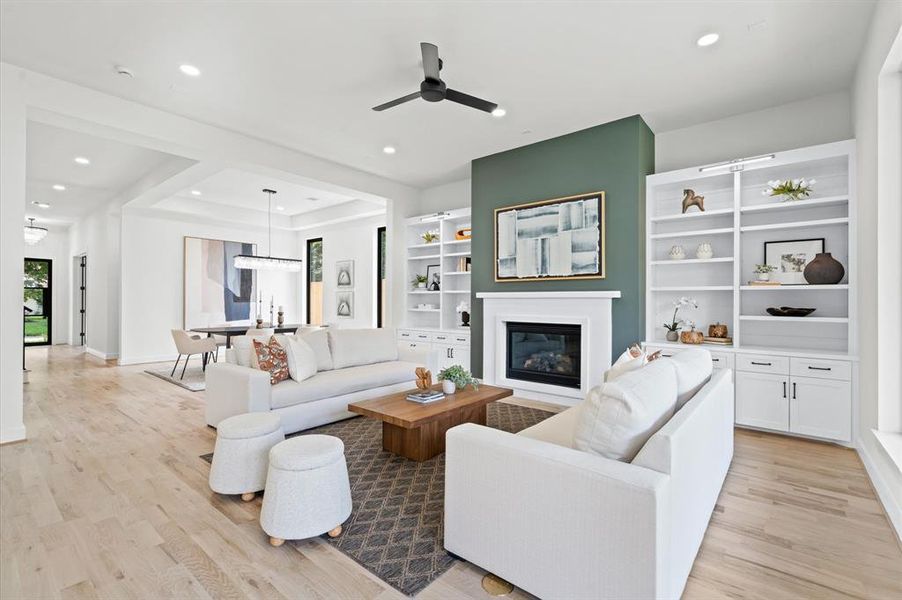 Spacious living room with white built-ins, fireplace, stone mantle; opens to a dining area with large windows, modern decor, and neutral tones.