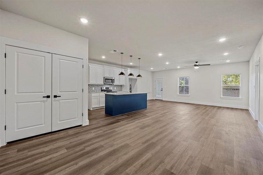 Kitchen with wood-type flooring, a kitchen island with sink, white cabinets, appliances with stainless steel finishes, and decorative light fixtures