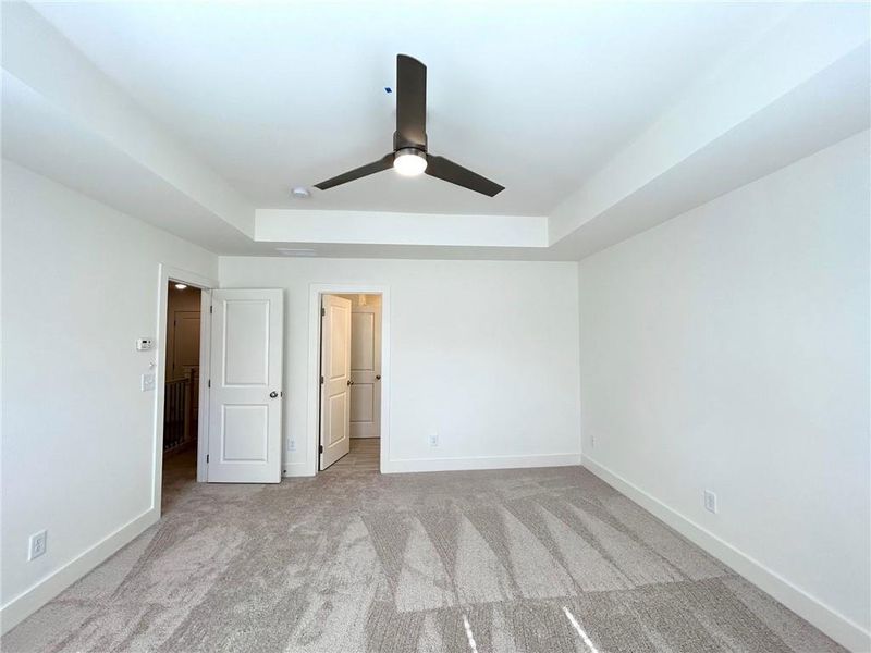 Unfurnished bedroom with light colored carpet, ceiling fan, and a tray ceiling