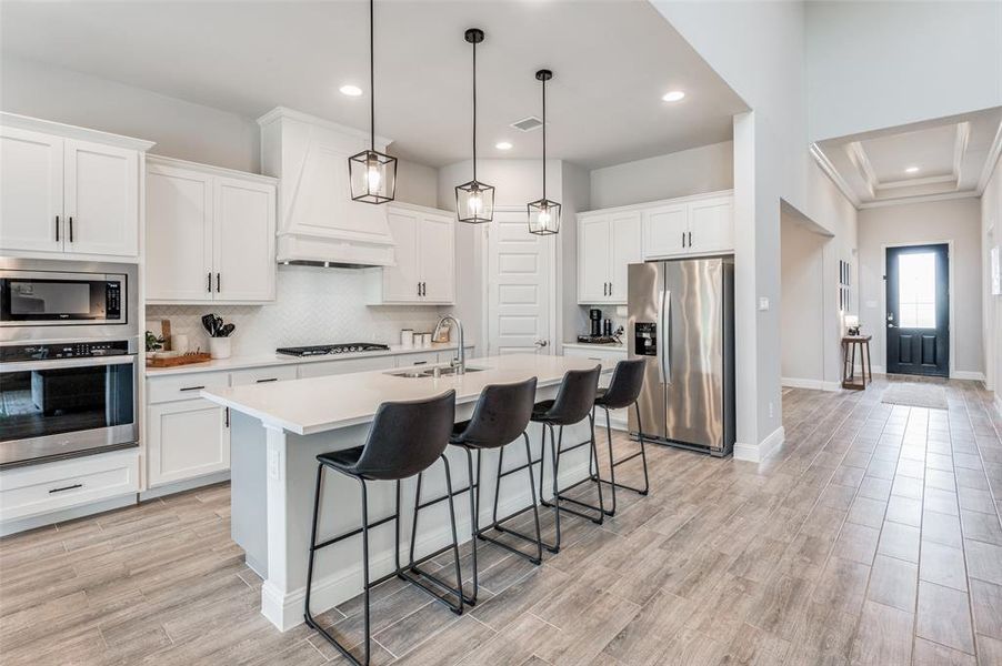 Kitchen with appliances with stainless steel finishes, tasteful backsplash, a center island with sink, light wood-type flooring, and custom range hood