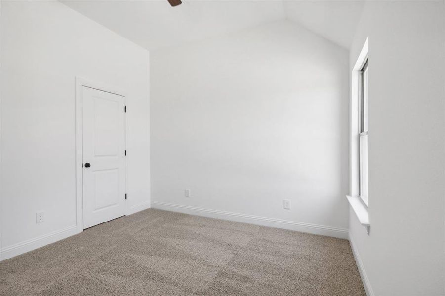 Carpeted empty room featuring vaulted ceiling and ceiling fan