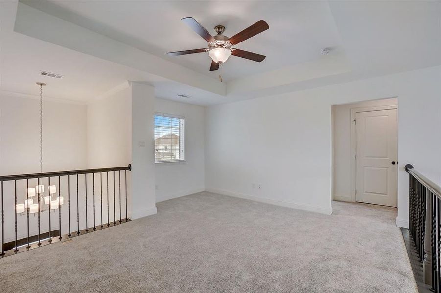 Unfurnished room with light carpet, a raised ceiling, and ceiling fan with notable chandelier