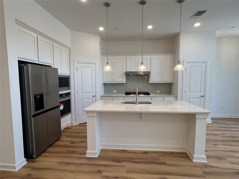 Kitchen with white cabinets, light hardwood / wood-style floors, tasteful backsplash, and stainless steel appliances